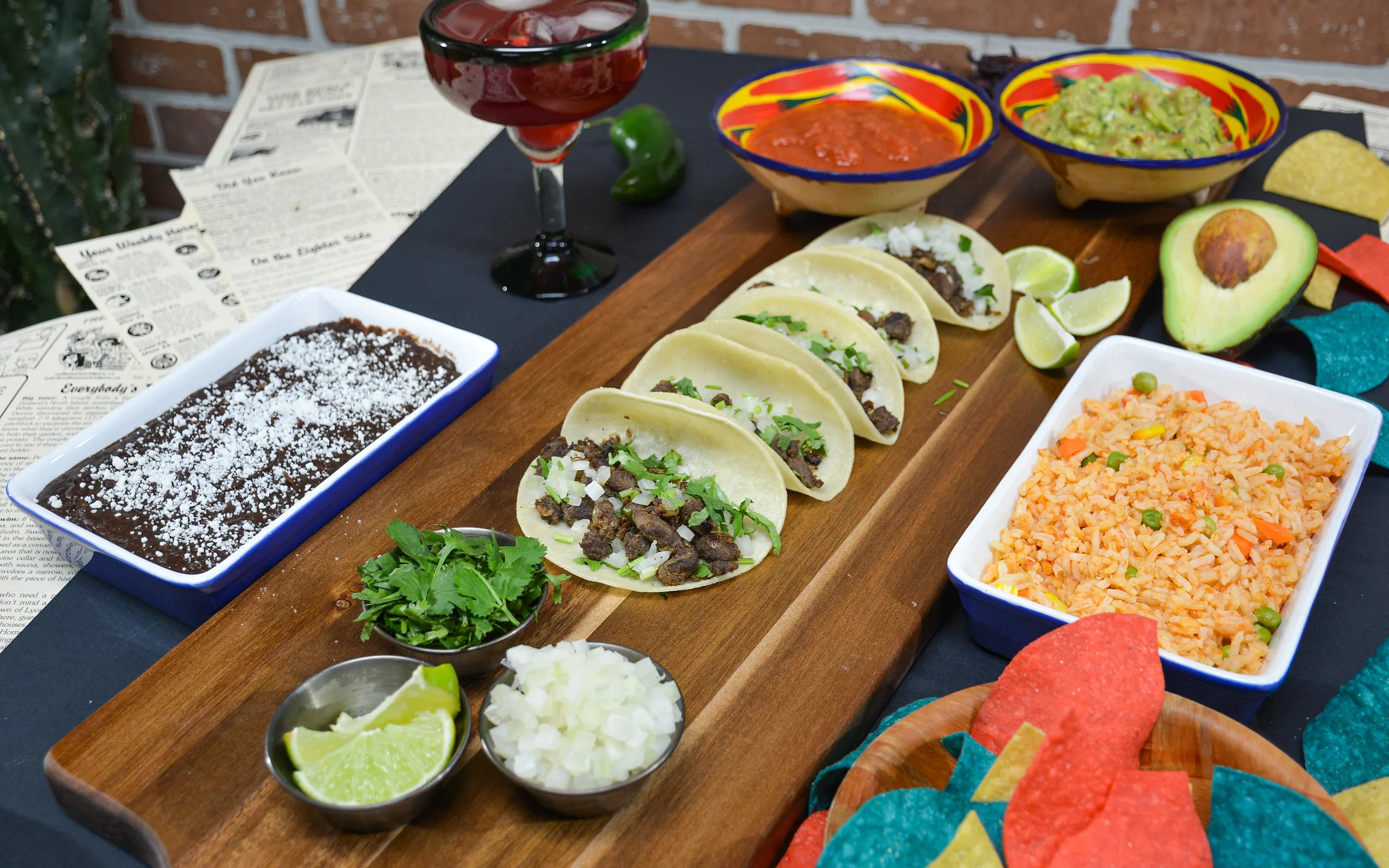 Hot tacos with cilantro and onion on a wooden board with black beans, Mexican rice, salsa, guacamole and tortilla chips from Tres Marias in Calgary